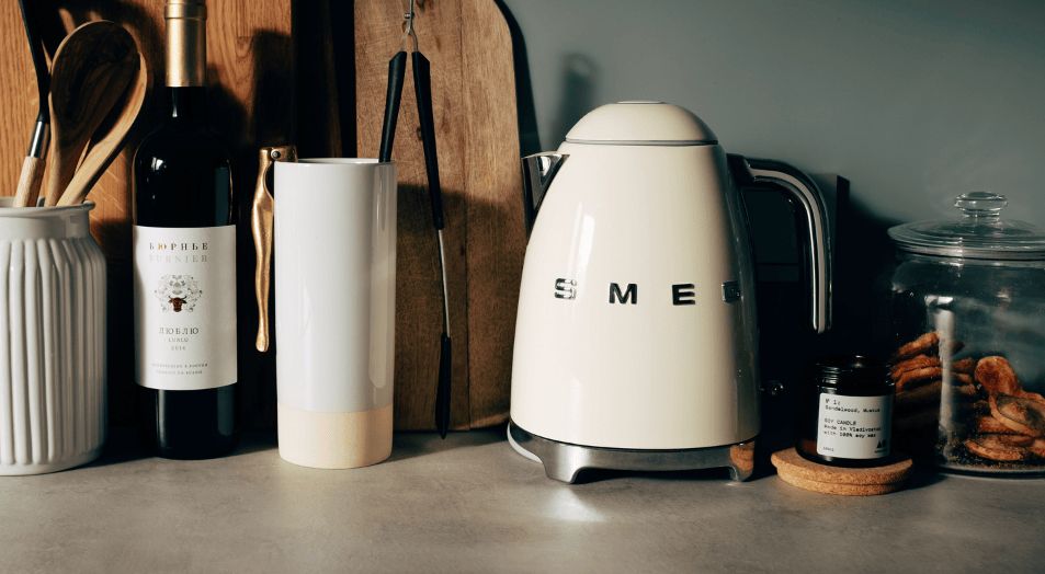 Una pava eléctrica Smeg color blanco con otros utensilios de cocina