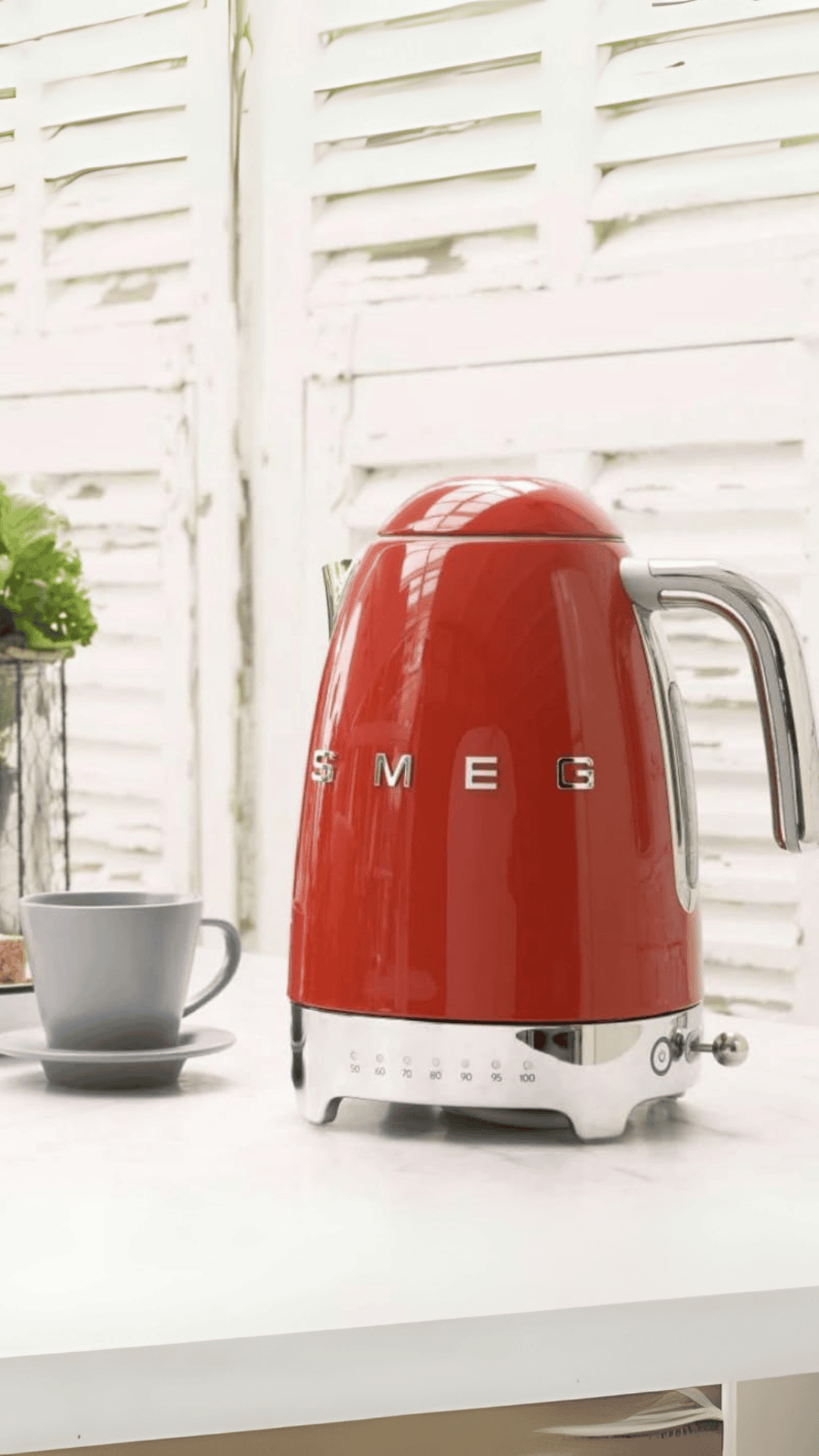 Pava Eléctrica SMEG roja con una taza gris al lado sobre una mesa