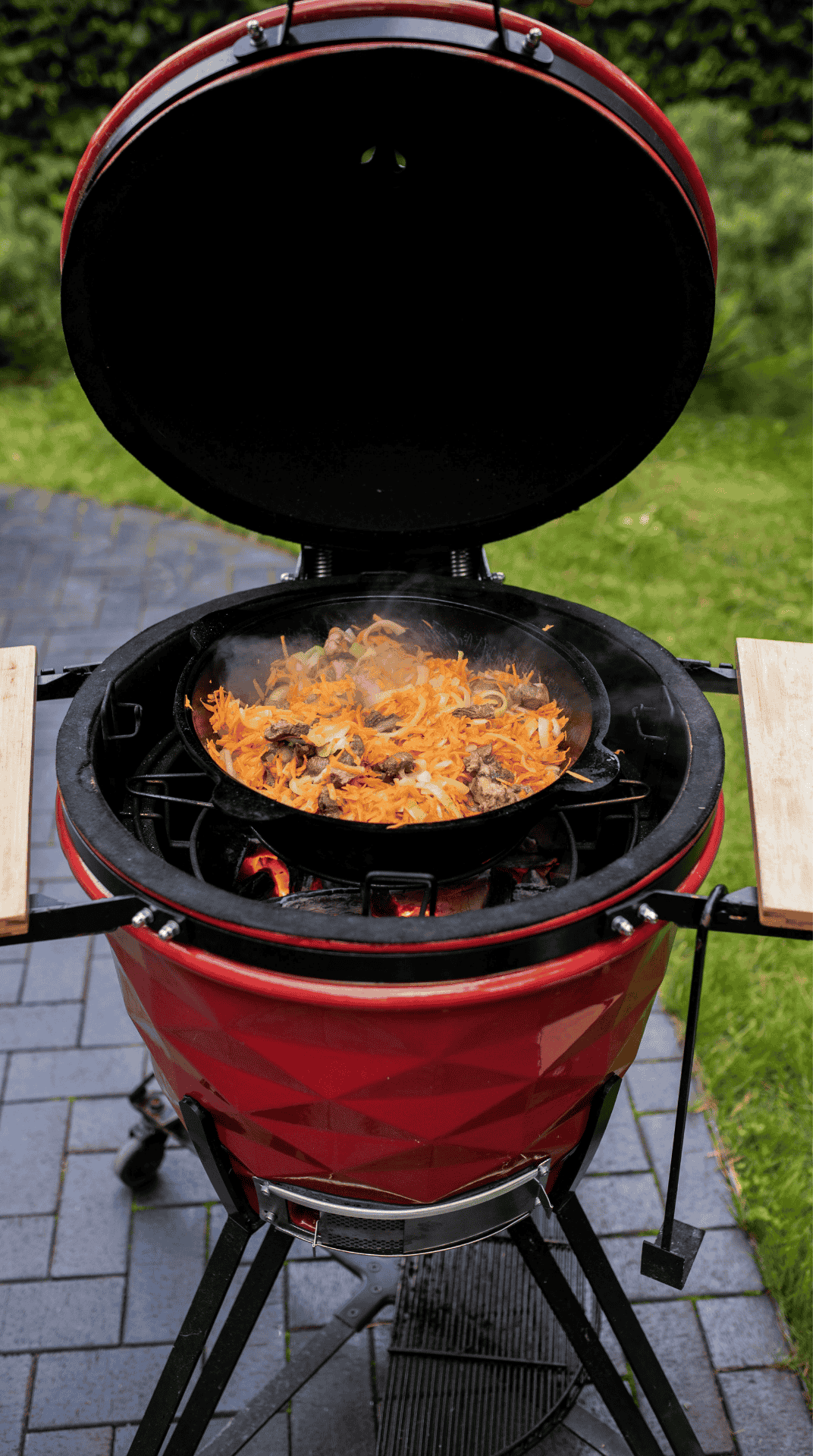 Kamado rojo con la tapa abierta y una paella haciéndose dentro