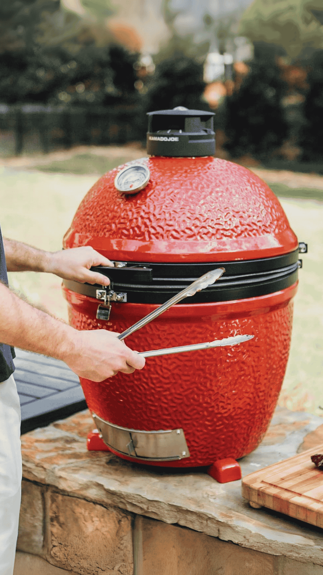 Kamado rojo apoyado sobre una mesa con unas manos abriéndolo
